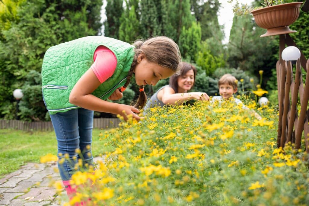 Kleines Mädchen mit Familie im Garten, die sich gemeinsam um die Pflanzen kümmern